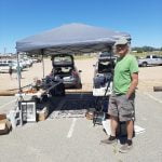 Anza swap meet vendor showcase: John Yarrow is a familiar face Man besides tent in parking lot with goods underneath
